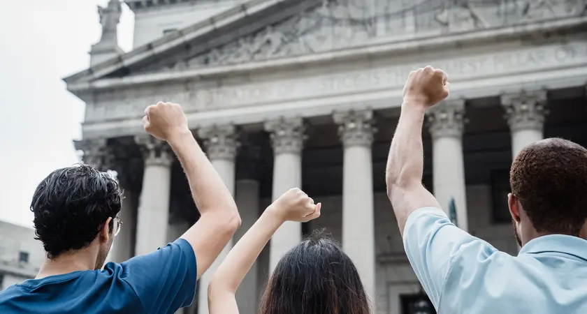 Three people raise their fists outside the Supreme Court building.