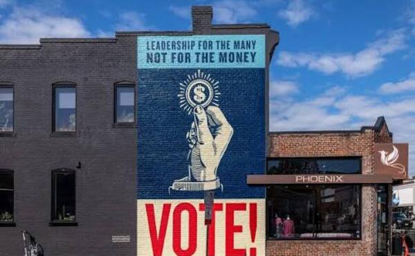 A photo of a mural on a brick wall that reads "Leadership for the many, not for the money. VOTE!"