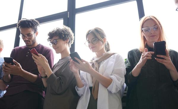 Four young poeple looking at their phones in front of a window