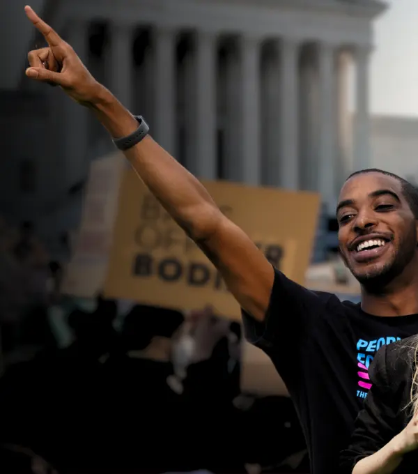 a white woman holding a megaphone and a Black man pointing to the sky at a rally