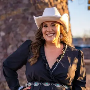 Selina Barajas wearing a black dress and white hat.