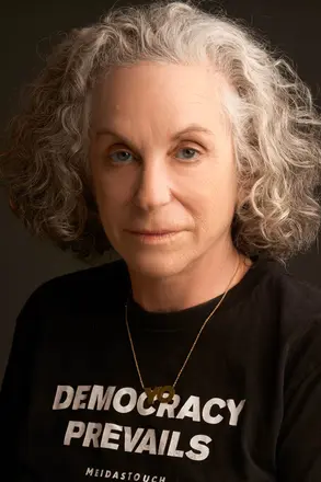 A photo of Deborah Kass, a woman with gray hair and a black shirt that says "Democracy prevails"