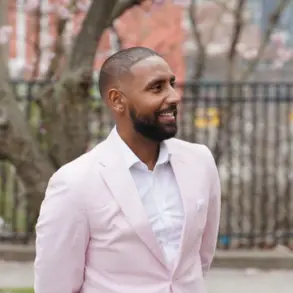 Mussab Ali wearing a pink jacket and standing on the sidewalk