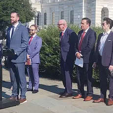 Photo shows Rep. Clay Fuller (R-GA) standing outside the US Capitol at a lectern with a sign that says "End SPLC Hate." Lined up behind him are five other people who spoke at the press conference, four men and one woman. 