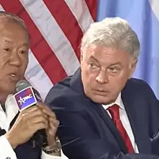 Che Ahn speaks into a microphone branded with a CPAC logo; seated to his left and listening to Ahn is Lance Wallnau.