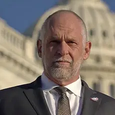 IFA President David Kubal, a balding white man in suit and tie, looks sternly into the camera with the US Capitol dome visible behind him. 