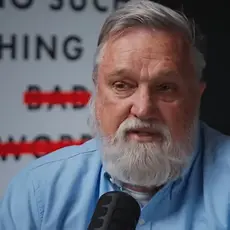 Doug Wilson, a middle-aged white man with gray hair and beard, is seated and speaking into a microphone. Partially visible behind him is an image of the cover of his book, "No Such Thing as Bad Words"