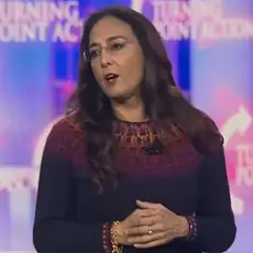 Harmeet Dhillon speaking from stage at Turning Point USA's AmericaFest conference in December 2024, with Turning Point Action logos visible behind her. 