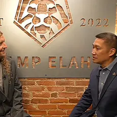 MAGA musician Sean Feucht and then-Senate candidate Hung Cao are seated in front of a brick wall on which is huge a large sign identifying their location as "Camp Elah," the Capitol Hill outpost for Feucht's political activities.