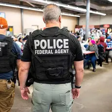 Photo shows several officers identified as police and/or ICE from the back as they face workers gathered in what appears to be a workplace lunchroom