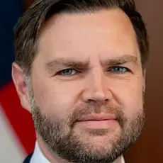 Close-up photo portrait of J.D. Vance with a blurry US flag visible behind him 