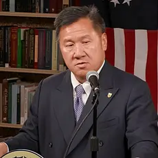 James Ho, in a suit and tie, speaks at a lectern with a U.S. flag visible behind him