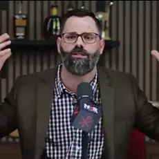 Joel Webbon gestures with both hands while seated behind a microphone that displays the logo for his NXR (New Christian Right) Studios