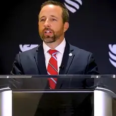 Josh Buice (pronounced Bice) in suit and tie stands at lectern in front of background bearing logo of the right-wing group Sovereign Nations