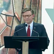 House Speaker Mike Johnson pictured standing at a lectern on the outdoor stage at the Rededicate 250 event.