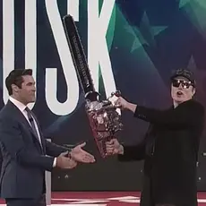 Elon Musk on stage at CPAC brandishing a chain saw. 