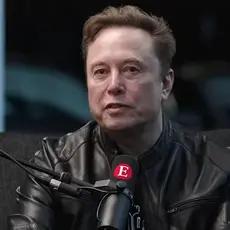 Elon Musk, in black shirt and leather jacket, is seated at a microphone that is emblazoned with a capital letter E, the logo for The Economist magazine