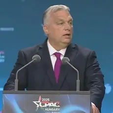 Viktor Orban stands at a lectern with logo for CPAC Hungary 2025, the logo is also visible on the backdrop behind him. 
