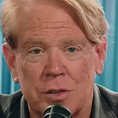 Close-up image of white man with reddish blonde hair speaking into a microphone.