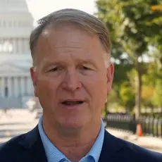 Phillip Jauregui is speaking into the camera while standing outdoors with the U.S. Capitol visible behind him. 