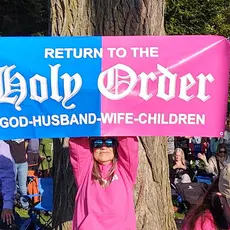 Participant in Oct. 12 rally holds a banner reading "Return to the Holy Order: God-Husband-Wife-Children"