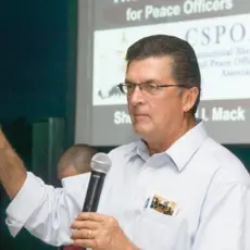 Photo of Richard Mack holding a microphone and pointing while speaking to an audience 
