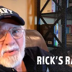 Rick Joyner, a white man with gray beard and mustache wearing a blue baseball cap with NAVY written on it, speaks into the camera while seated in an easy chair. 