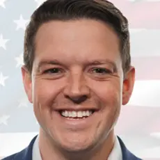 Portrait photo of Ryan Helfenbein, a smiling white man with faded US flag image in background
