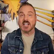 Shawn Bolz, a white man with short brown facial hair, sitting in a tshirt and jean jacket in an informal office setting with bookshelves visible behind him