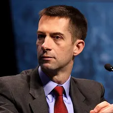 Photo of Sen Tom Cotton in suit and red tie seated at a microphone.