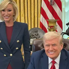 Donald Trump is seated at his desk in the Oval Office, with White standing next to and slightly behind him, both smiling for the camera. Partially visible behind White is a map on an easel touting the "Gulf of America."
