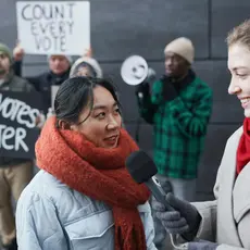 A reporter with a microphone interviews voting rights protestors