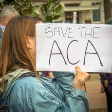 A woman holds a sign that says "Save the ACA"