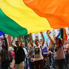 A group of people hold onto a massive rainbow flag