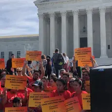 Activists stand outside the Supreme Court wearing red and carrying signs that read "America needs a fair and accurate #2020Census."