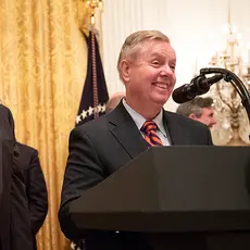 Lindsey Graham stands behind a podium with Donald Trump at his side.