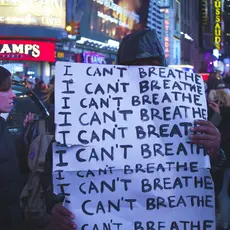 A man holds a sign in a crowded city; the sign says "I can't breathe. I can't breathe. I can't breathe."