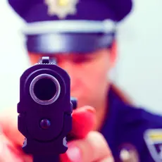 A police officer aims a gun directly at the camera
