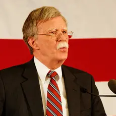 John Bolton stands at a podium in front of an American flag