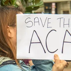 A woman holds a sign that says "Save the ACA"