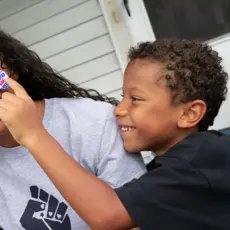 A Black son places an "I Voted" sticker on his mother's smiling face.