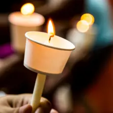 Hands holding candles with paper wax protectors.