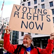A man holds a cardboard sign that reads Voting Rights Now