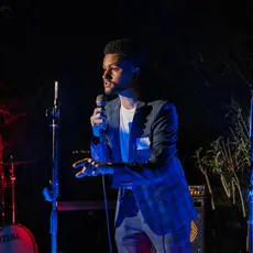 Rep. Maxwell Frost holds a microphone and speaks on a stage with musical equipment.