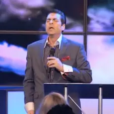 Hank Kunneman holding a microphone and standing at a podium.