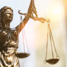 A photo of a statue of lady justice holding scales with sunlight in the background.