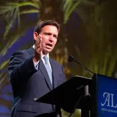 Ron DeSantis standing in front of a podium that says "ALEC" on it.