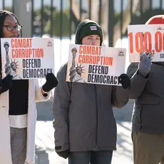 Three people hold signs reading "combat corruption, defend democracy"